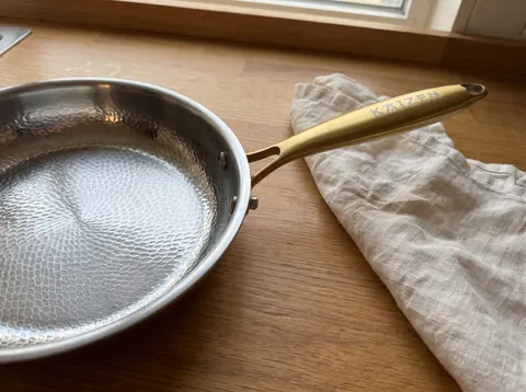 Close view of the Kaizen pan surface pattern, curved rim and gold handle attachment